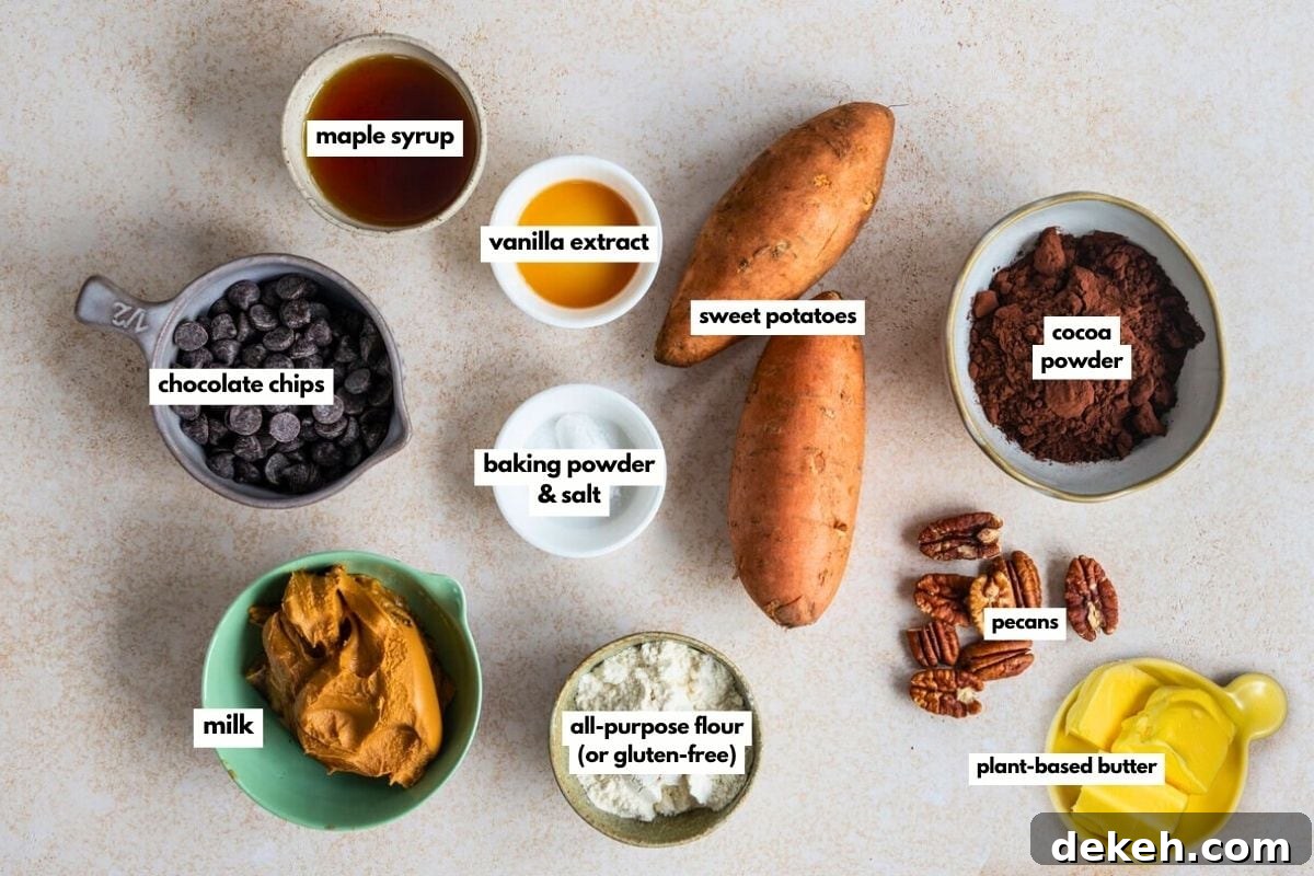 Top-down view of labeled ingredients for vegan sweet potato brownies on a countertop: maple syrup, vanilla extract, sweet potatoes, chocolate chips, cocoa powder, baking powder & salt, pecans, milk, all-purpose flour, peanut butter, and plant-based butter.