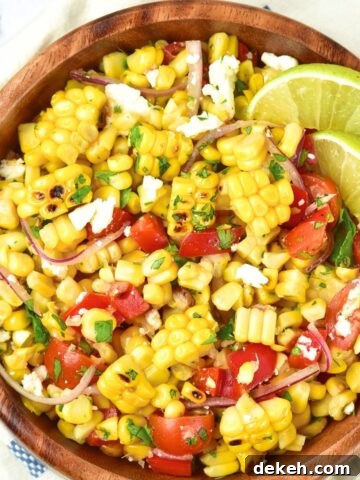 Top down view of a bowl of grilled corn salad with lime wedges.