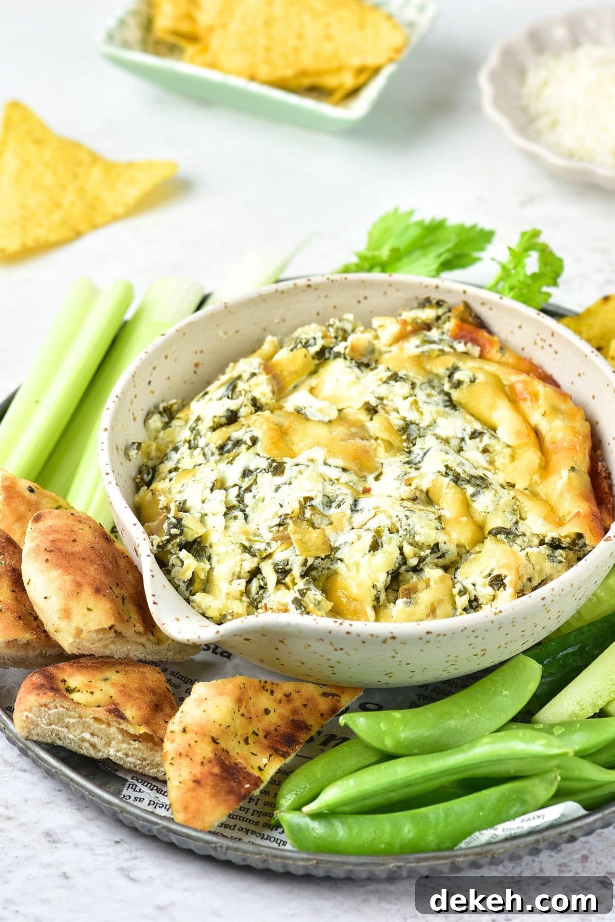 A bowl of spinach and artichoke dip with pita chips and raw veggies