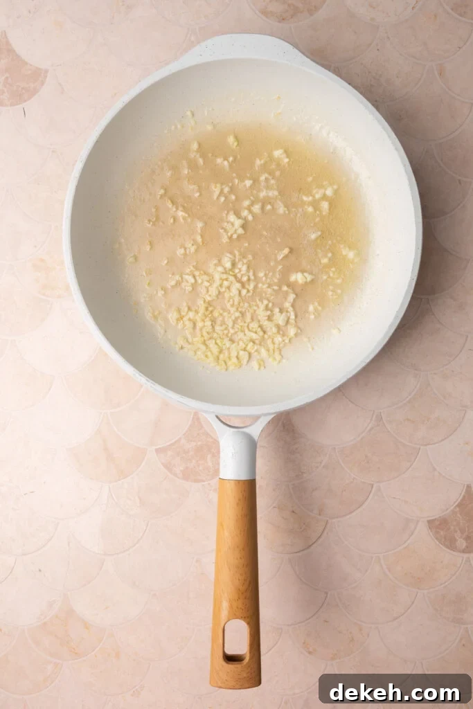Minced garlic cooking in butter in a white pan.