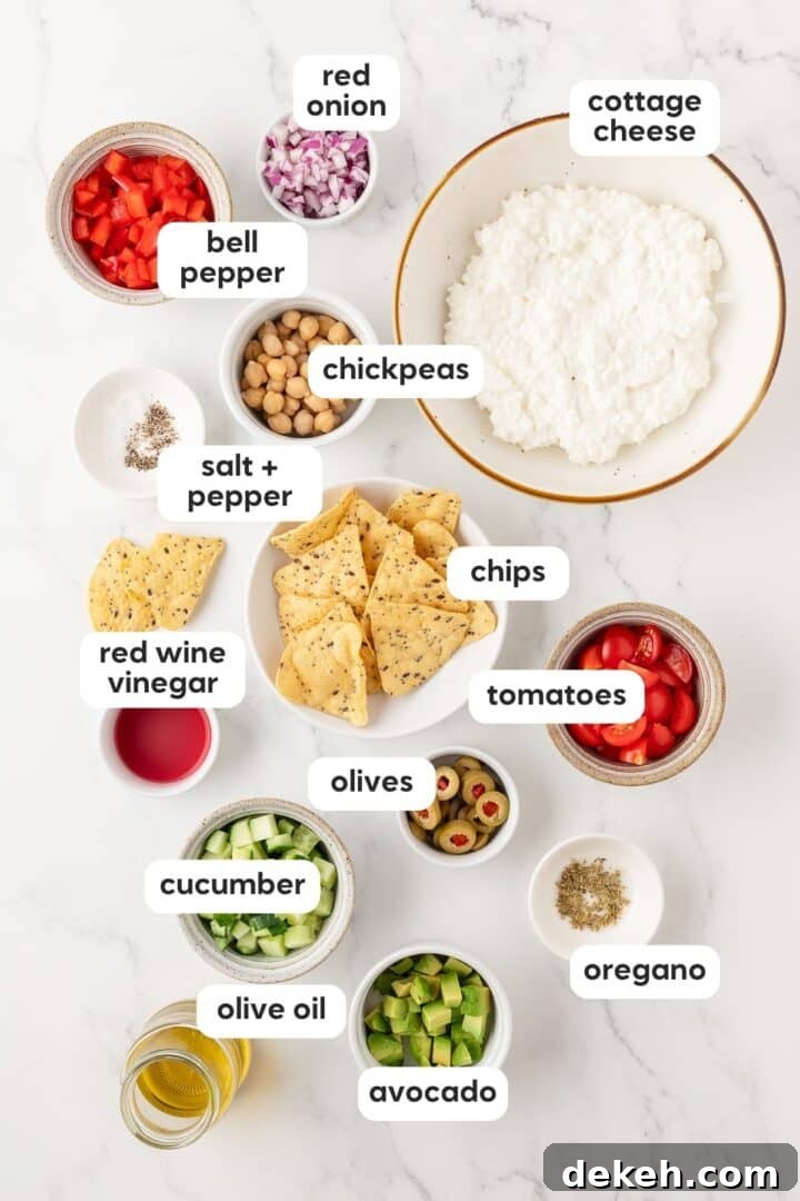 Ingredients for cottage cheese greek salad displayed in small bowls on a white marble counter.