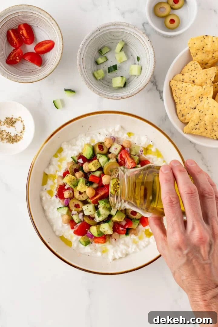 Woman's hand pouring olive oil over a cottage cheese greek salad in a white bowl.