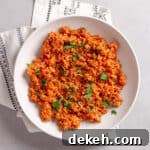 A serving of bulgur pilaf in a white bowl topped with chopped fresh herbs.