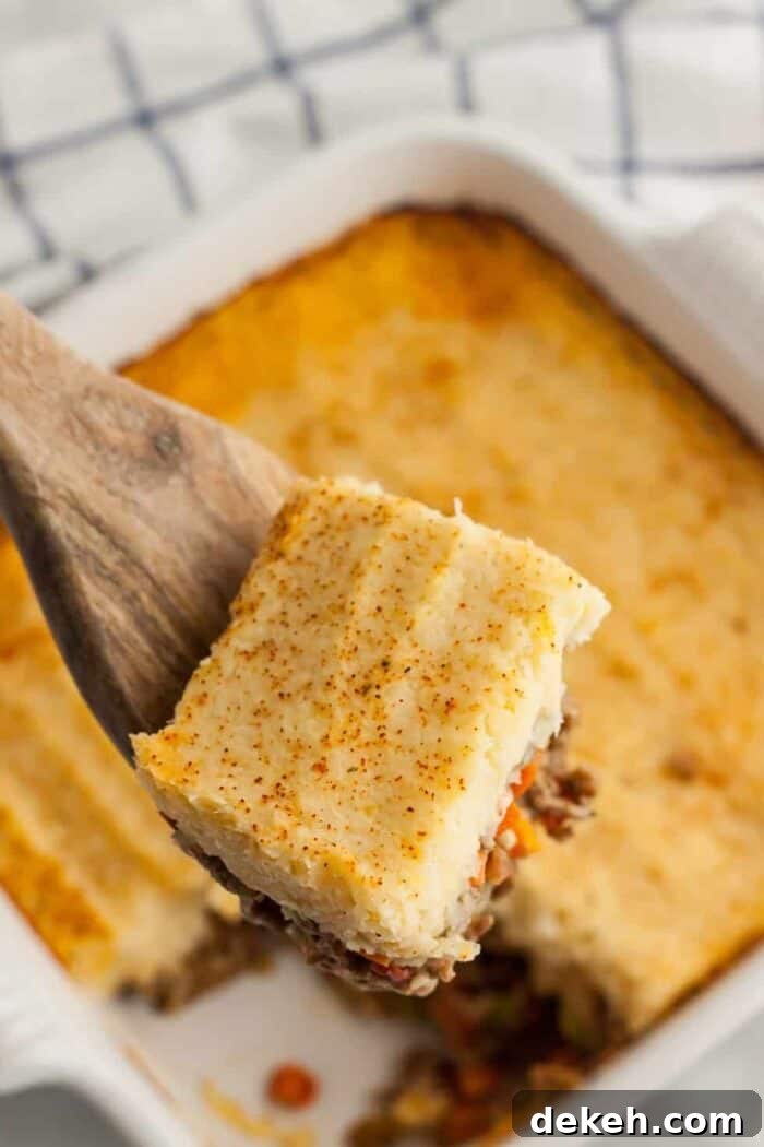 spoon holding up slice of keto shepherd's pie above a casserole dish