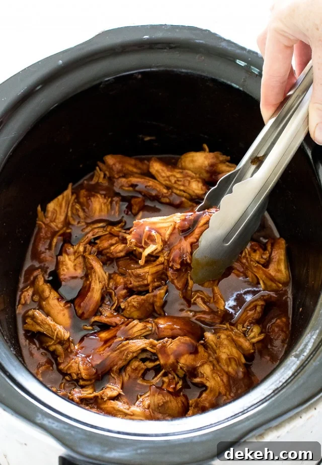 BBQ crockpot chicken with hands taking a portion with tongs. 