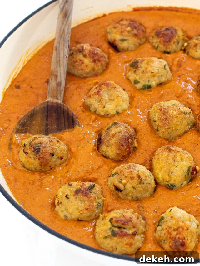 Butter chicken meatballs in a skillet with a wooden spoon. 