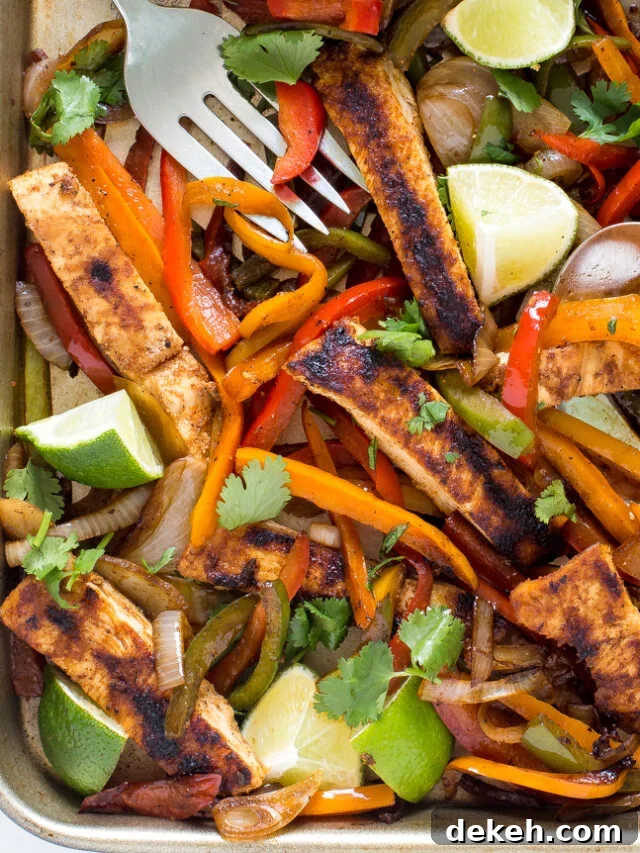 Chicken fajitas on a baking sheet with cilantro and lime wedges. 