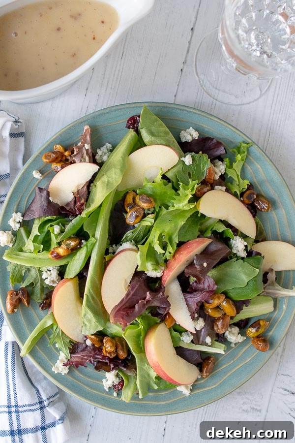an overhead shot of harvest salad on a blue plate with a wine class and container of dressing next to it