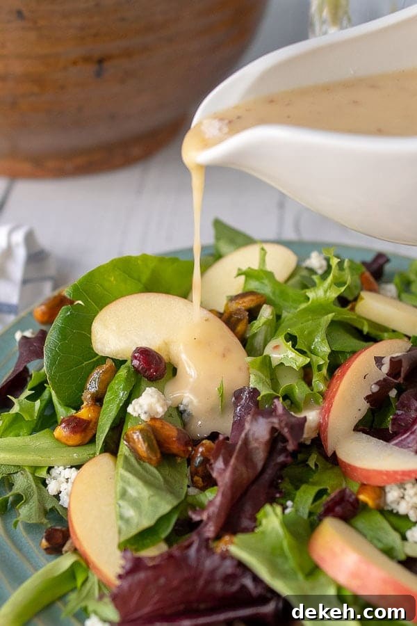 maple vinaigrette being poured from a white dressing container onto the harvest salad