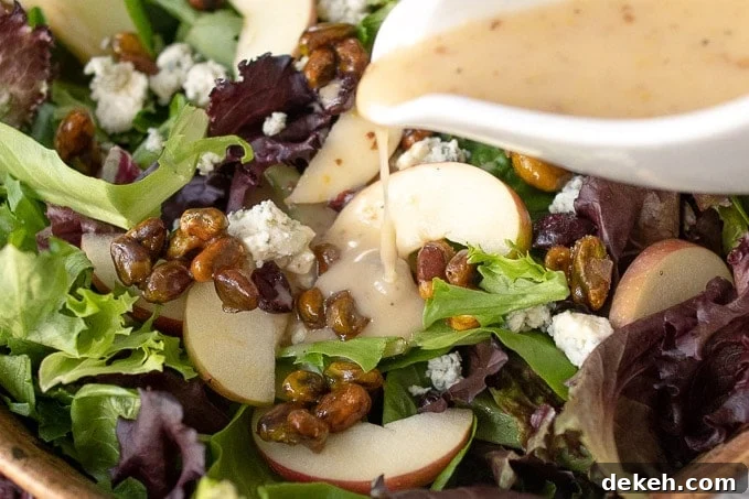 an up close shot of maple vinaigrette being poured from a white dressing container onto the harvest salad