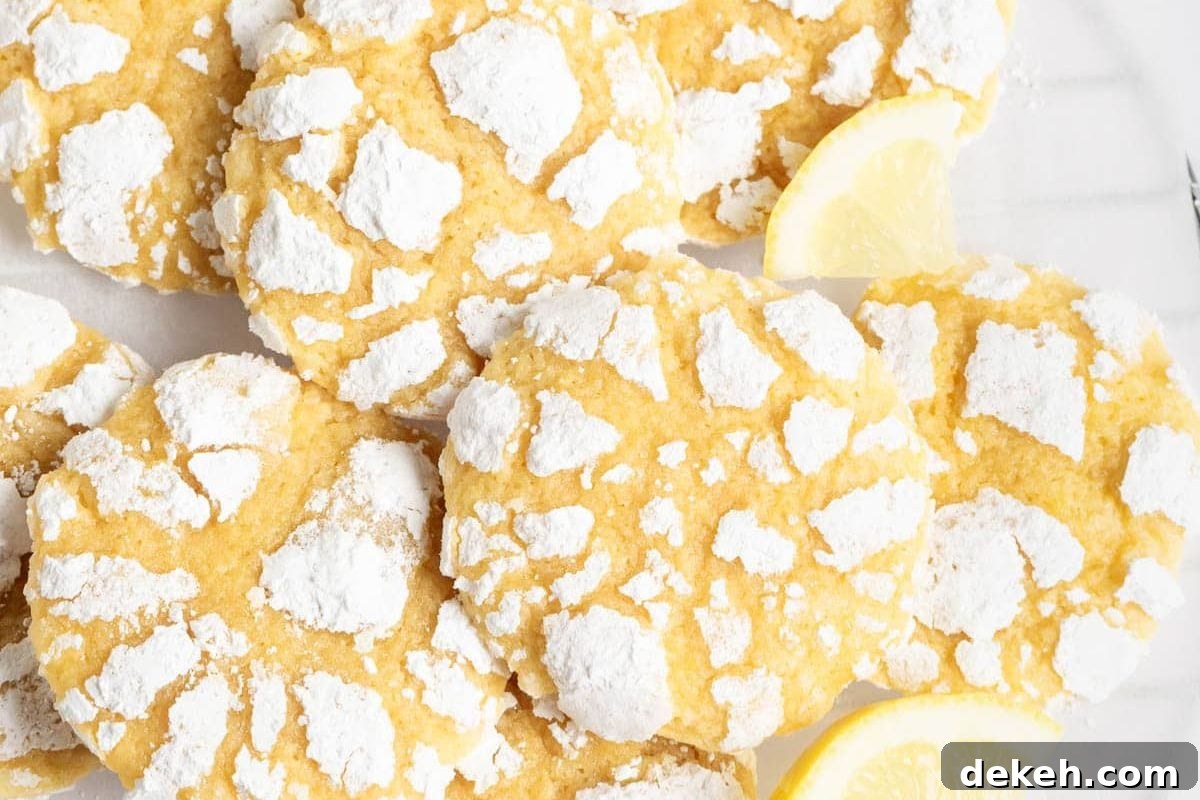 A close-up view of lemon crinkle cookies dusted with powdered sugar, accompanied by a slice of lemon on the side.