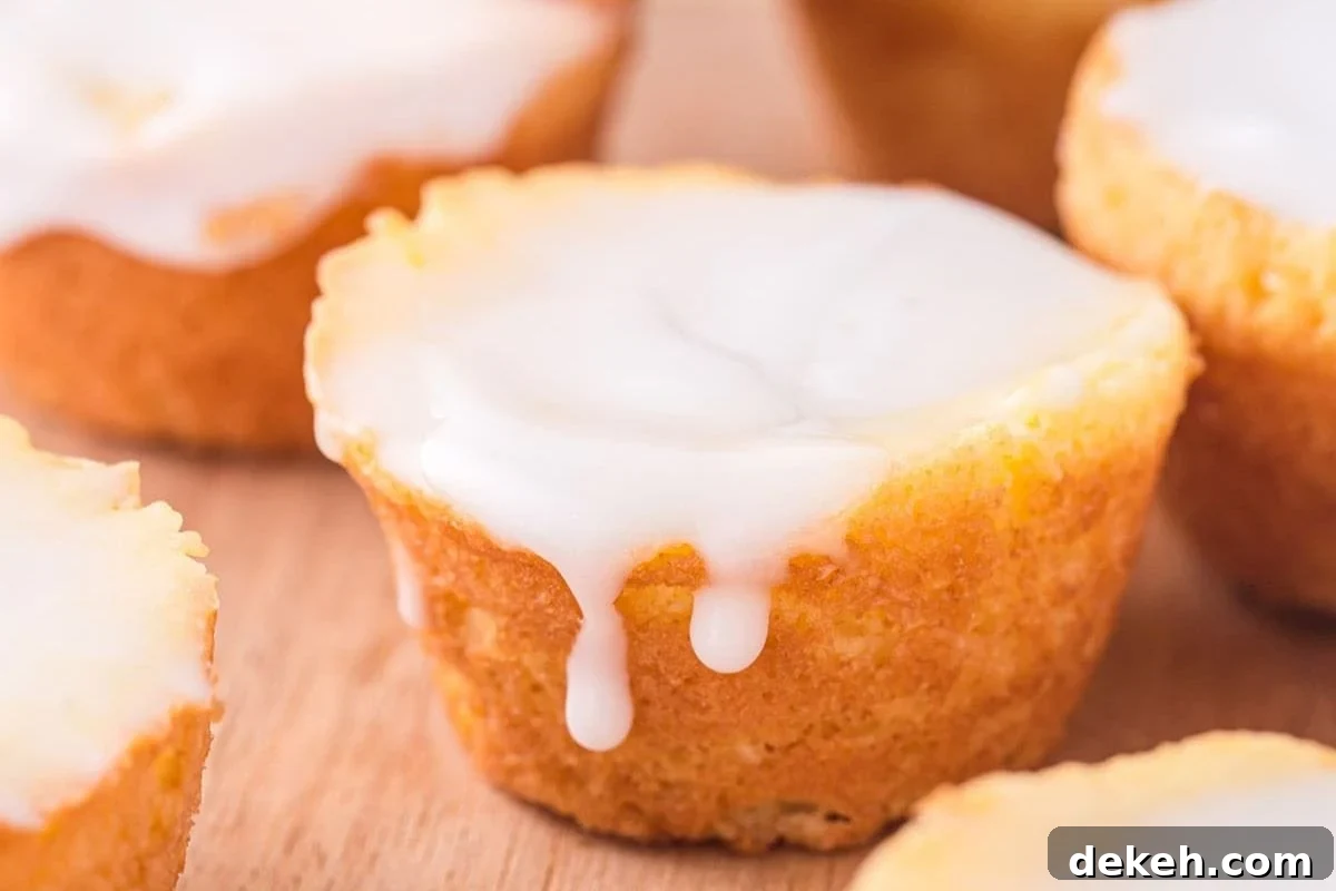 A close-up of freshly baked mini cupcakes topped with smooth white icing, some icing gently dripping down the sides, on a wooden surface.
