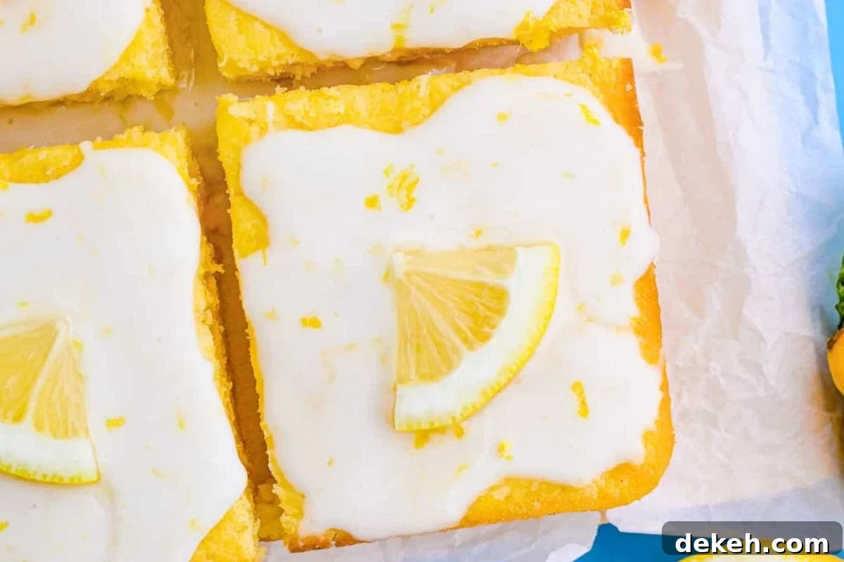 Delicious lemon bars topped with a glossy icing and a slice of lemon garnish, arranged neatly on parchment paper.