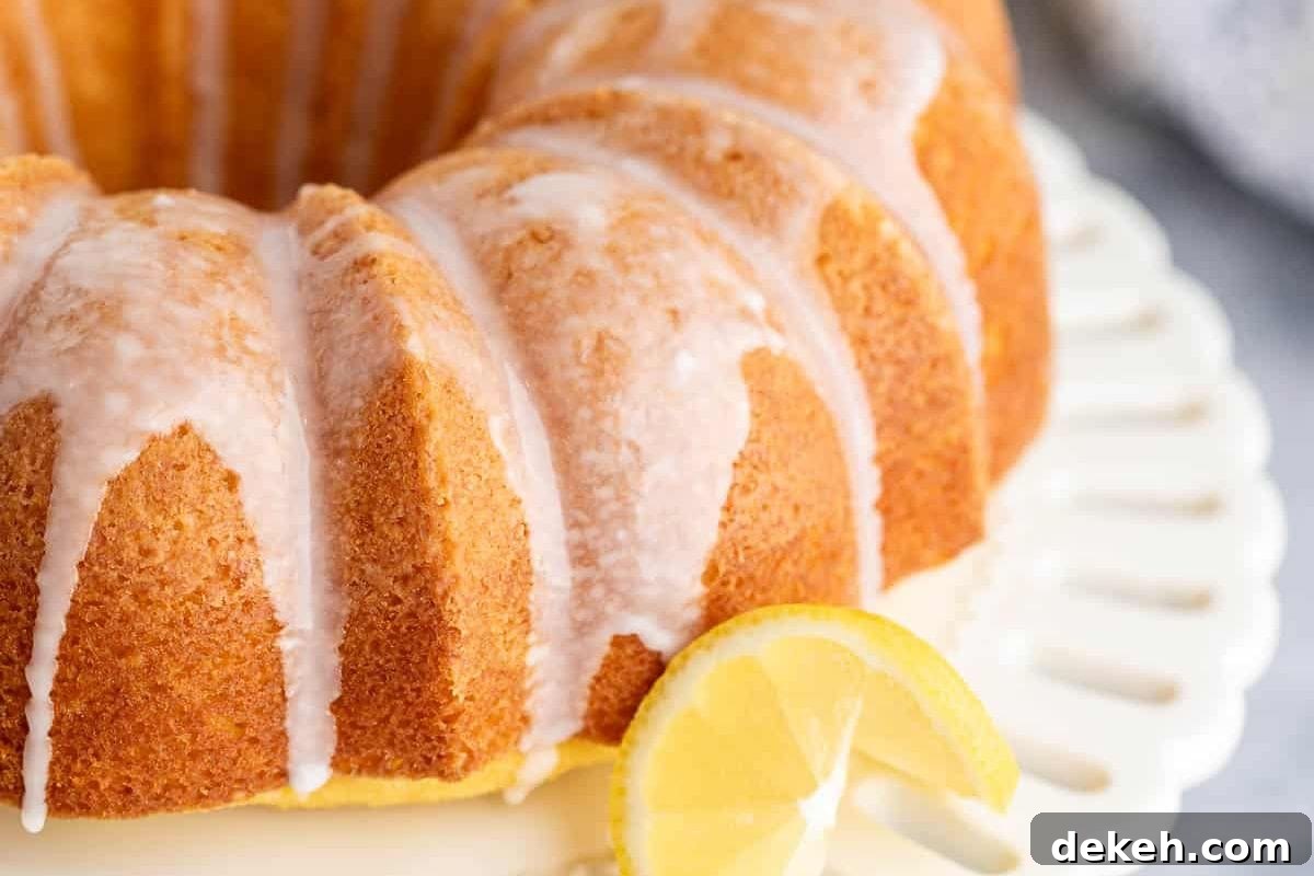 A close-up view of a moist lemon bundt cake topped with a glossy glaze, garnished with a slice of lemon on a decorative plate.
