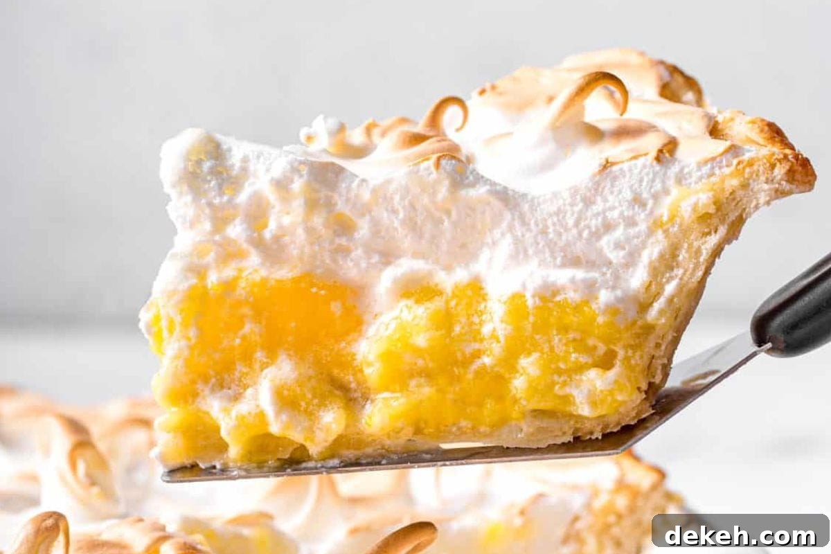 A close-up of a slice of lemon meringue pie being lifted by a serving utensil, showcasing the yellow filling and fluffy meringue topping.