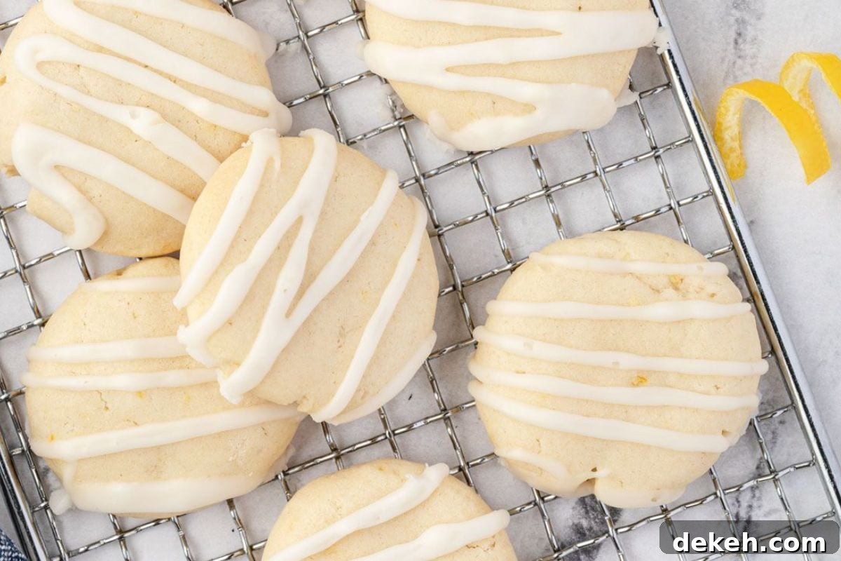 A close-up of soft lemon-flavored cookies drizzled with white icing, resting on a wire cooling rack.
