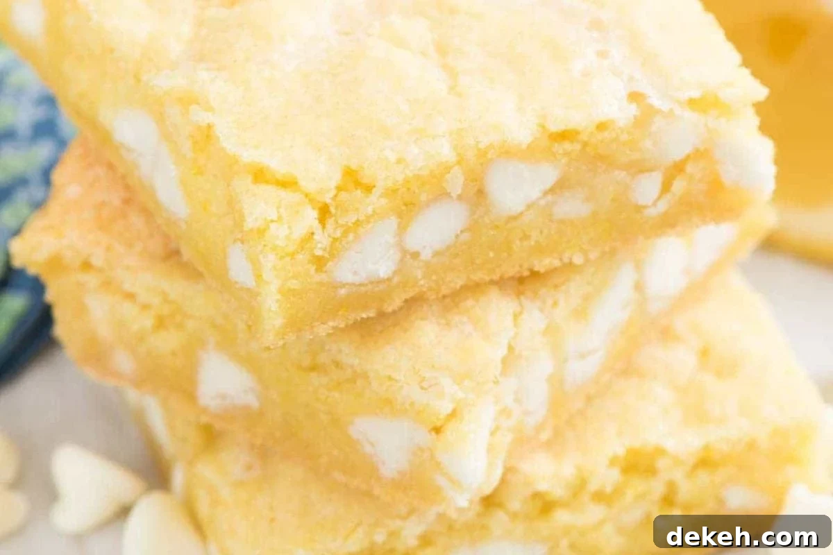 Close-up of stacked lemon-flavored bars with white chocolate chips, featuring a soft, yellow texture and a sprinkle of white chocolate pieces around them.