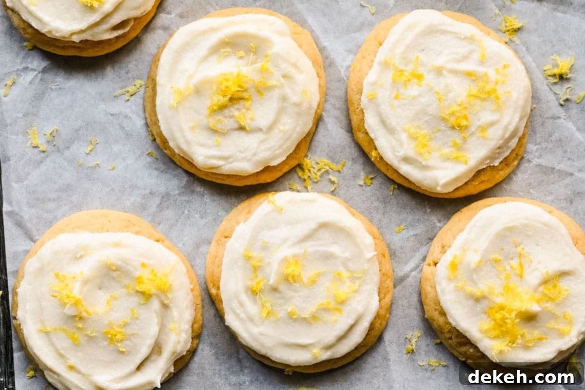 A close-up view of freshly baked lemon frosted cookies topped with yellow zest on parchment paper.