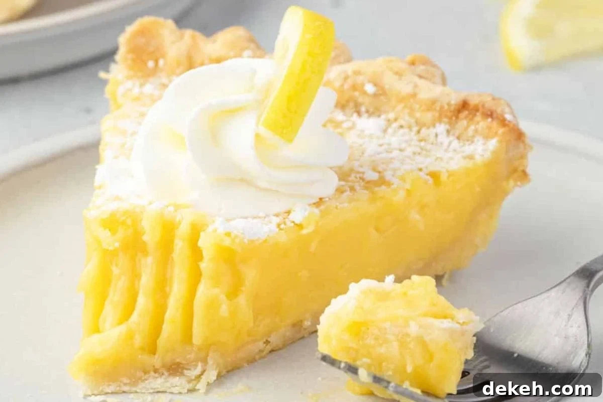 A slice of lemon meringue pie topped with whipped cream and a lemon slice, served on a plate with a fork and a piece cut out.