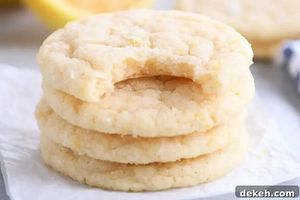A close-up of three soft lemon sugar cookies stacked, with one showing a bite taken out, on a parchment paper backdrop.