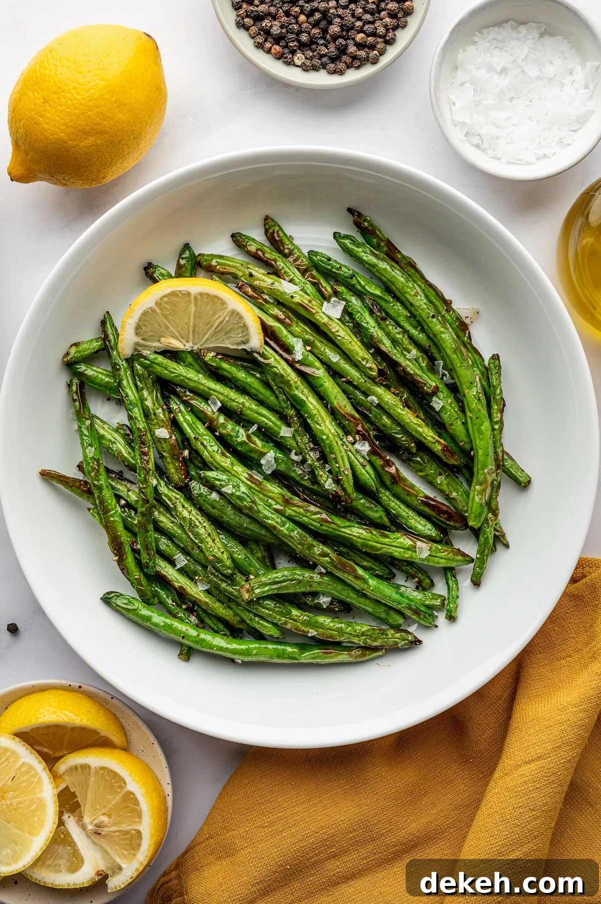 Cooked air fryer green beans served in a white bowl with lemon wedge and flaky salt.