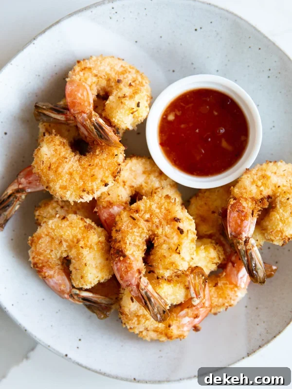 Overhead image of a serving plate filled with air fryer coconut shrimp and a small bowl of apricot dipping sauce.