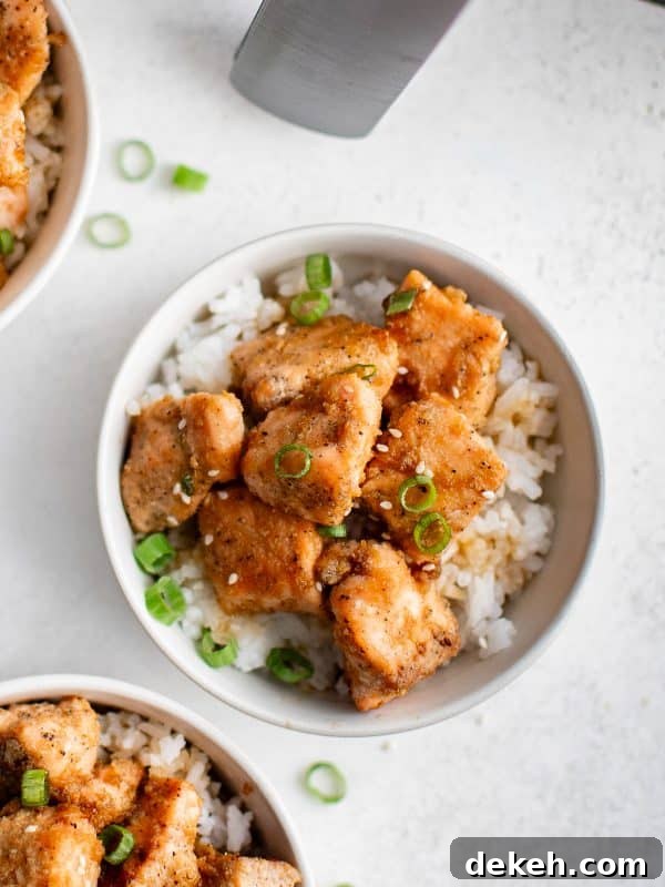 Overhead view of bowls filled with white rice and golden salmon bites, garnished with sesame seeds and sliced green onions.