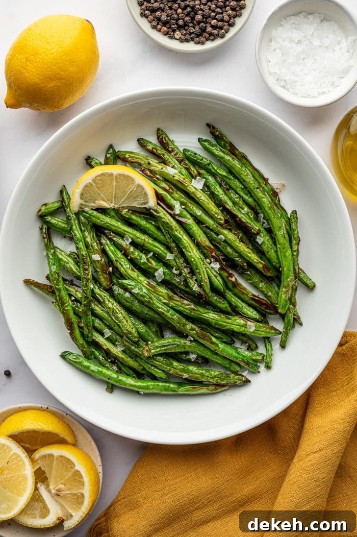 Cooked air fryer green beans served in a white bowl with lemon wedge and flaky salt.