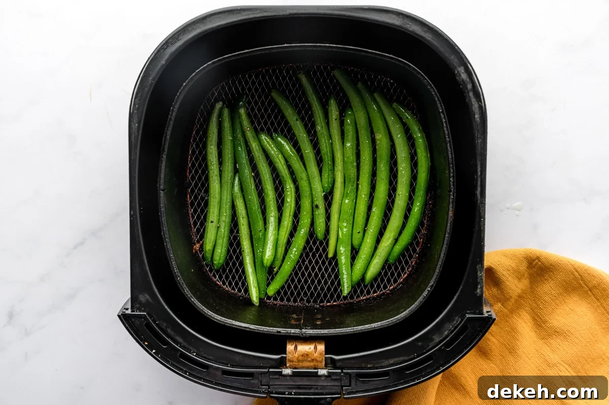 Raw green beans arranged in a single layer inside an air fryer basket.