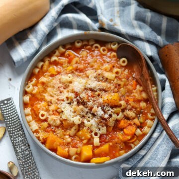 overhead view of a bowl of vegan pasta e fagioli soup with grated brazil nut and butternut squash.