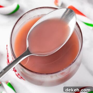 A spoonful of purple-pink Starbucks peppermint syrup, on a white marble table with candy cane pieces.
