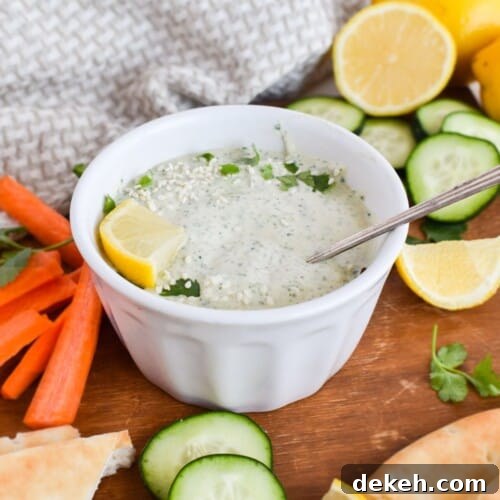 bowl of lemon herb tahini with vegetables on wooden board.
