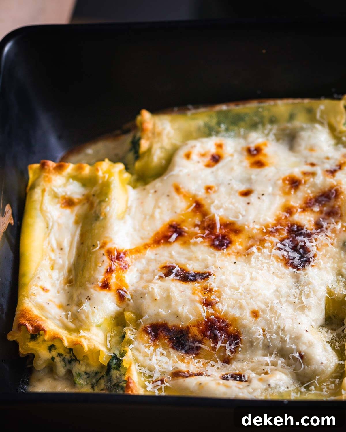 Spinach lasagna rolls with white sauce in black baking dish.