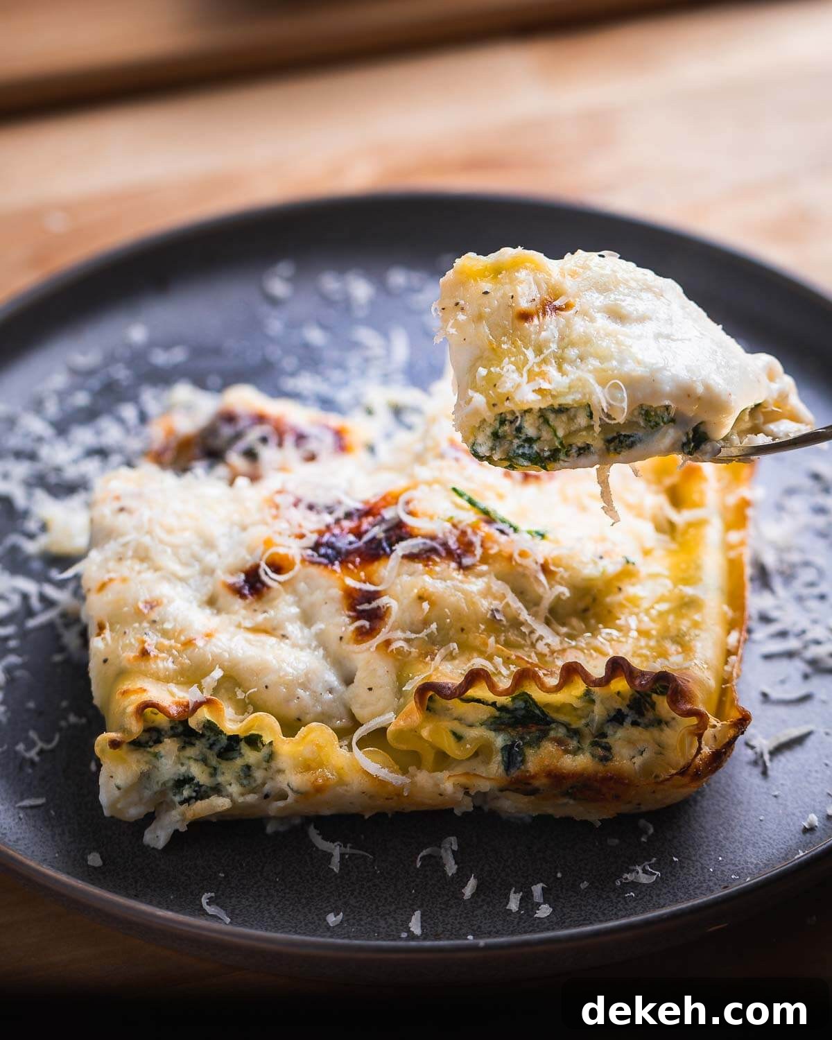 Cut piece of spinach lasagna roll up being held in fork.