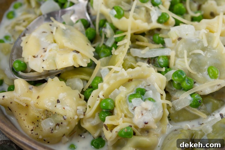 close up of cooked tortellini in a white sauce with peas and onions.