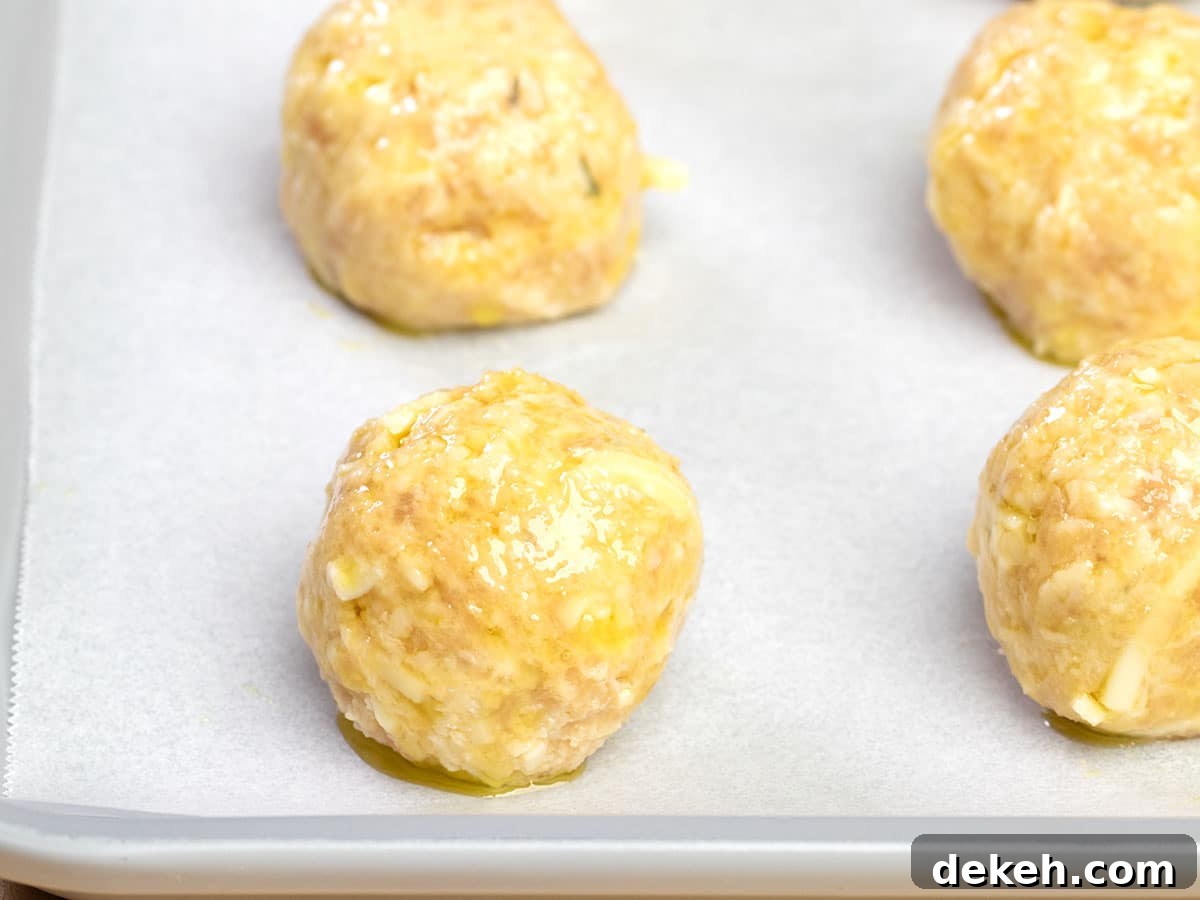 closeup image of 4 raw shaped baked chicken meatballs with olive oil on white paper