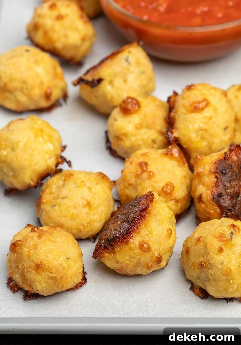 12 baked chicken meatballs on white paper on tray with small bowl of red tomato sauce