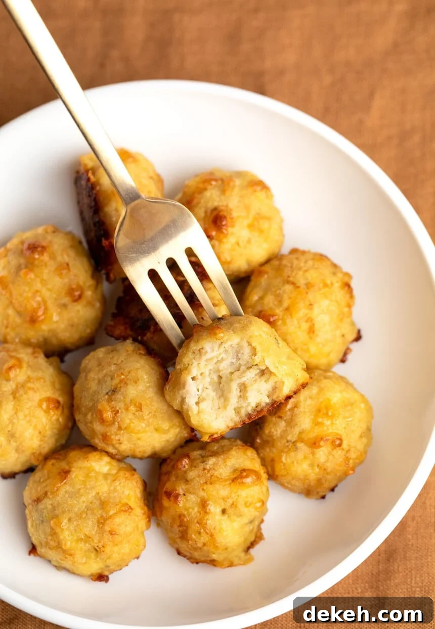 11 baked chicken meatballs in wide flat white bowl with gold fork with one meatball broken in half