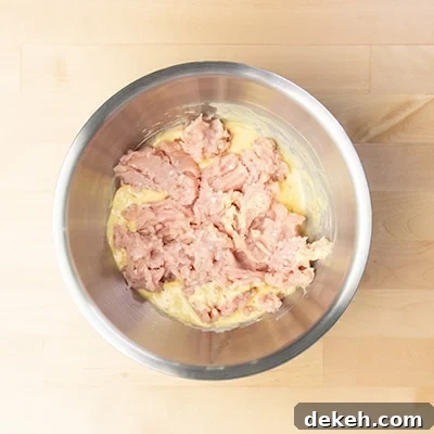 same mixing bowl with crumbled ground chicken on top of yellow liquid