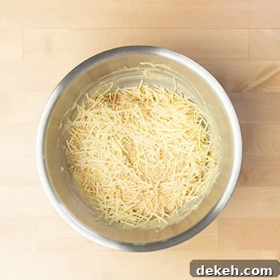 shredded parmesan cheese on top of chicken mixture in mixing bowl