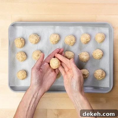 hands shaping raw chicken meatball mixture into rounds with fingers