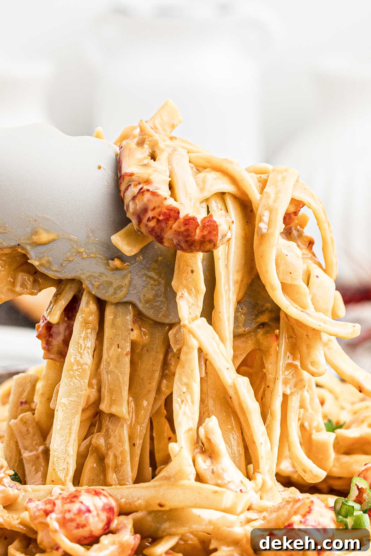 very close up view of tongs picking up crawfish fettuccine