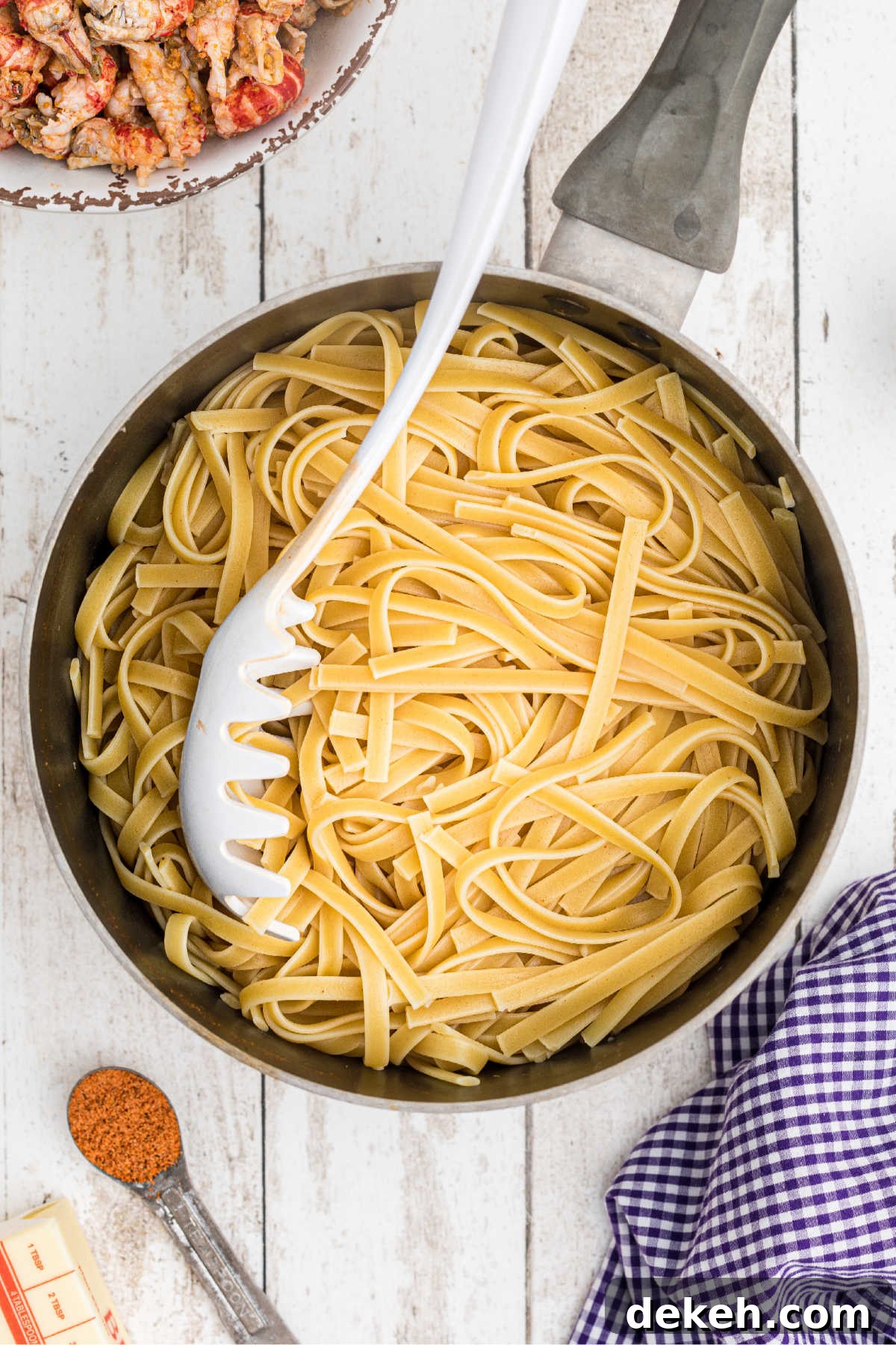 Cooked Fettuccine in a pot with a pasta spoon.
