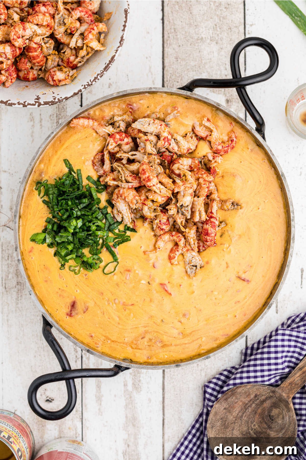 Crawfish tails and chopped green onions in a skillet with a cheesy sauce.