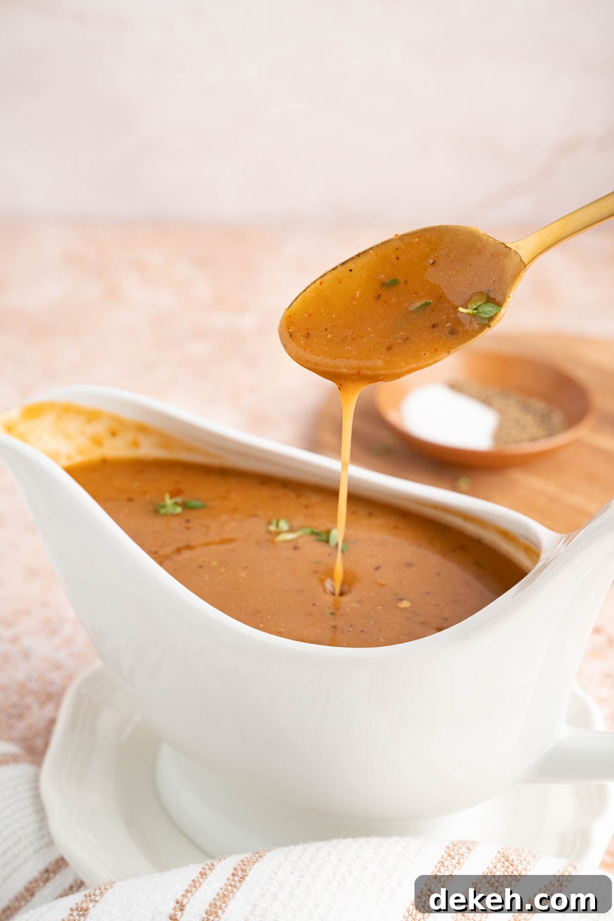 The turkey gravy made from drippings drips off a spoon held over a gravy boat. 