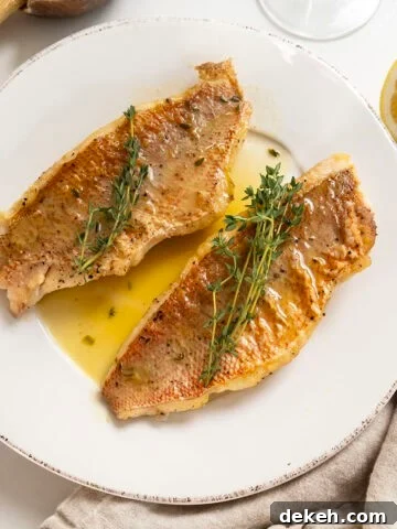 2 filets of pan seared vermillion snapper on a plate garnished with thyme sprigs.