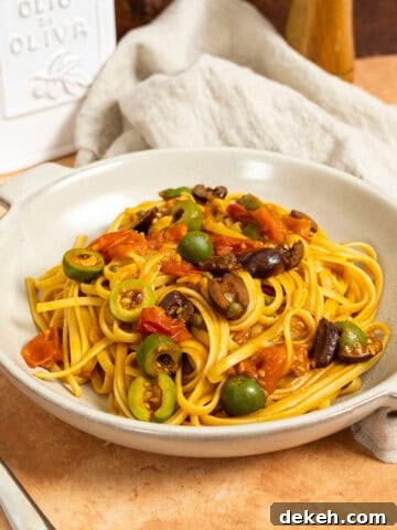 Linguine puttanesca topped with olives and capers in a bowl.