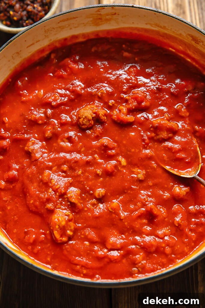 Top down shot of sausage ragu tomato sauce in a large pan with a serving spoon