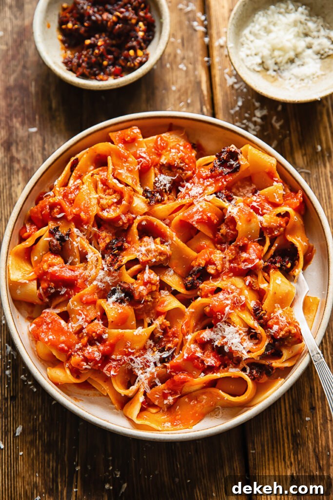 Top down shot of chilli crisp sausage ragu in a bowl with a fork topped with Parmesan