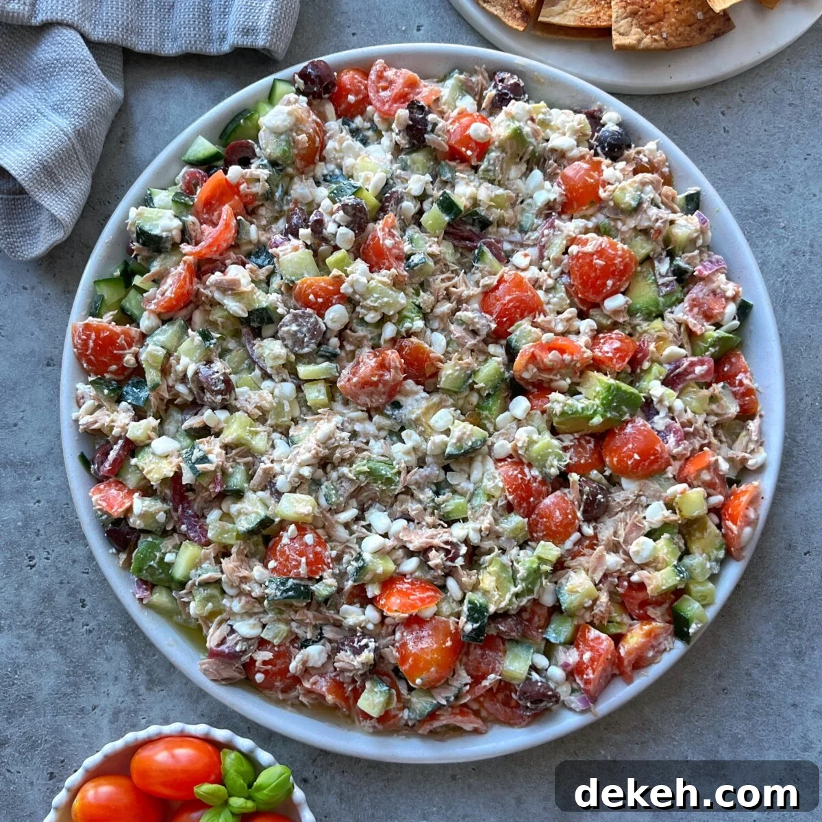 A large plate of Tuna Cottage Cheese Salad with cherry tomatoes, cucumbers, red onions, feta cheese, olives, and chunks of tuna mixed with dressing.